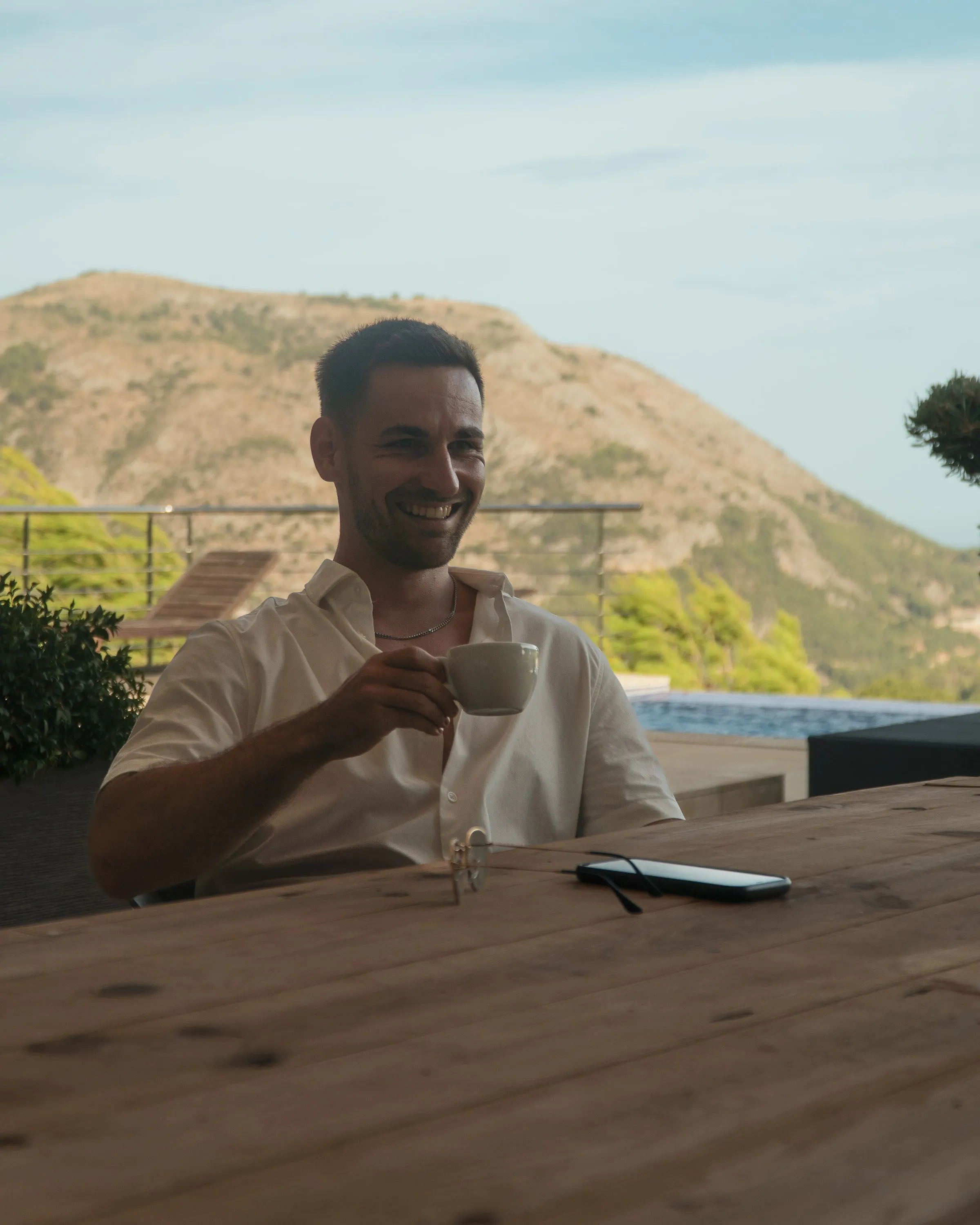Lorenz Edlinger bei einem Kaffee, im Hintergrund Pool und Berge
